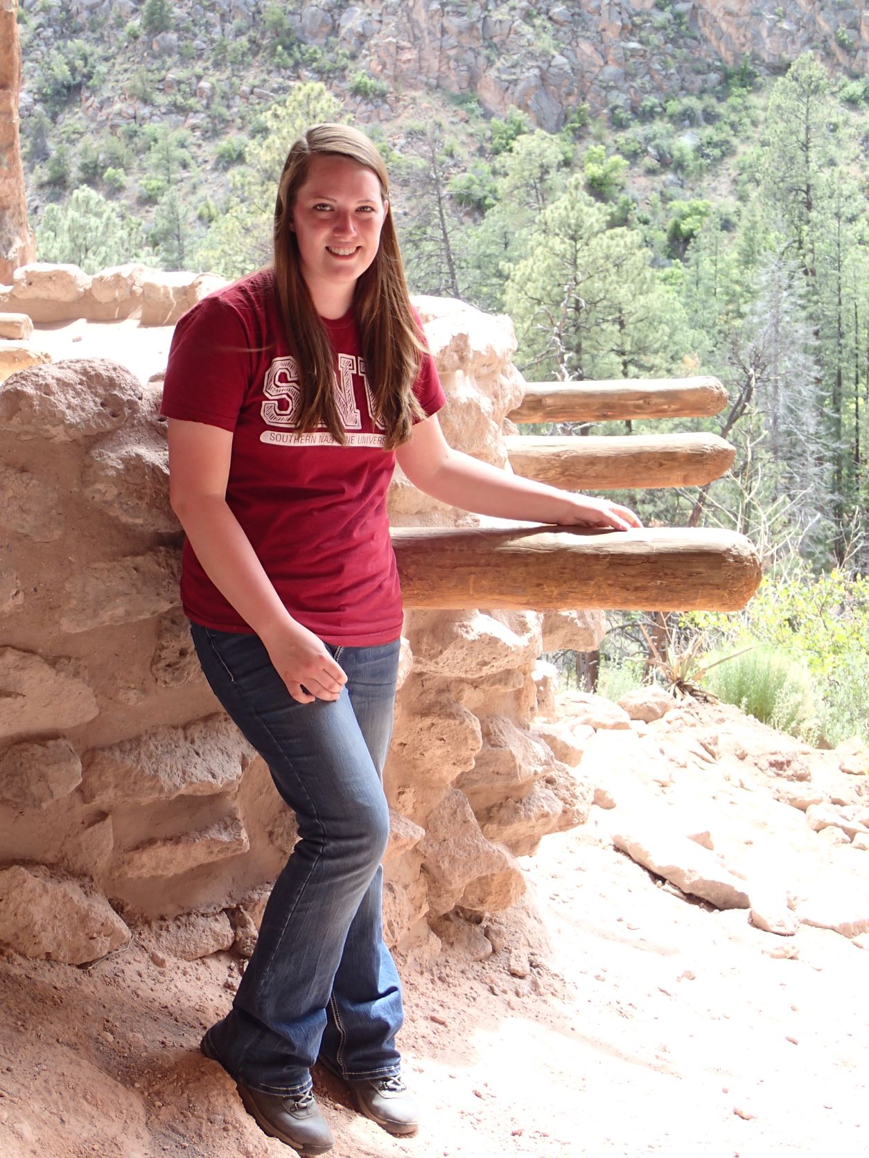 A girl standing by a rock formation with wooden posts sticking out from it.