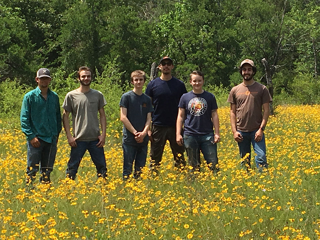 Six individuals standing in a valley full of yellow wild flowers.