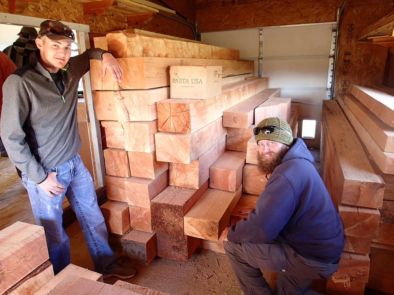 Two participants posing next to stacks of wooden logs.