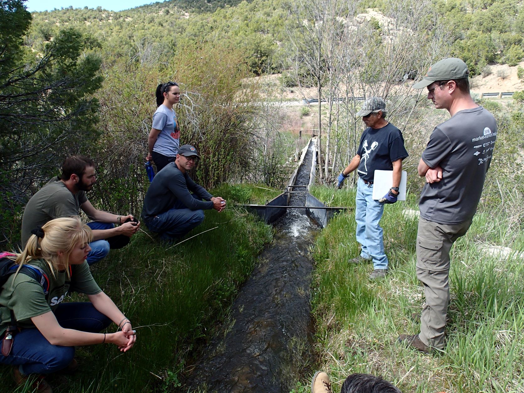 A group of five students and an instructor standing over a stream in the woods.