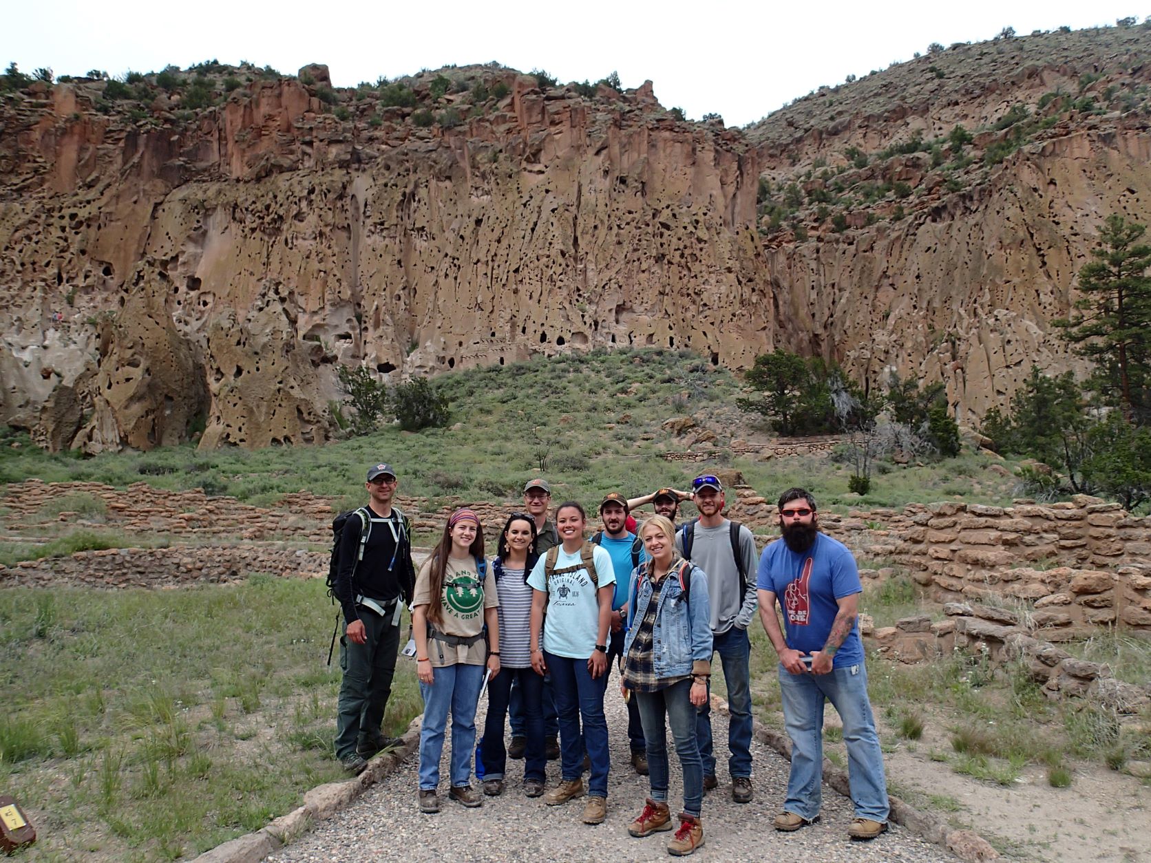 A group of 10 people standing on a path at the base of a large rocky cliff.