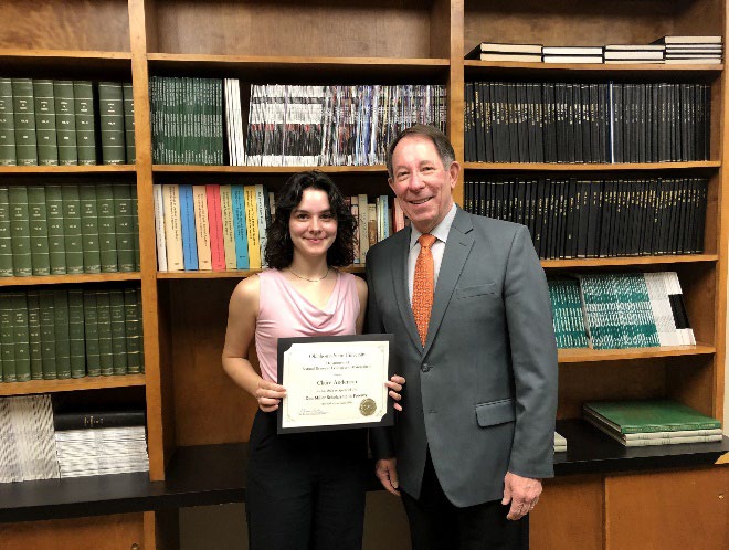 Claire Anderson is accepting her award from Jim Ansley in front of a book shelf.