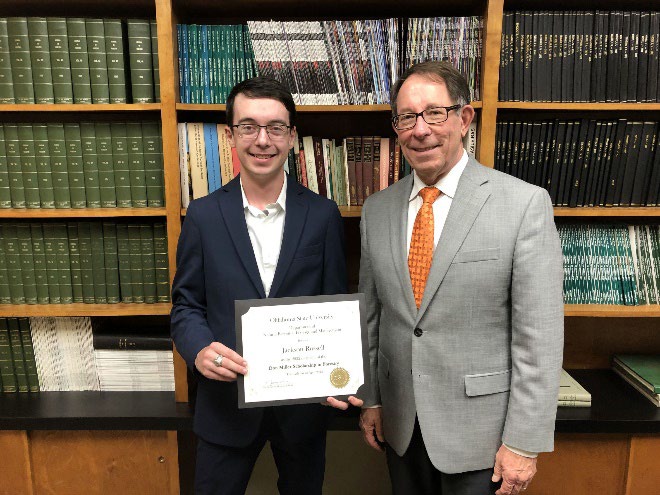 Jackson Russell is accepting his award from Jim Ansley in front of a book shelf