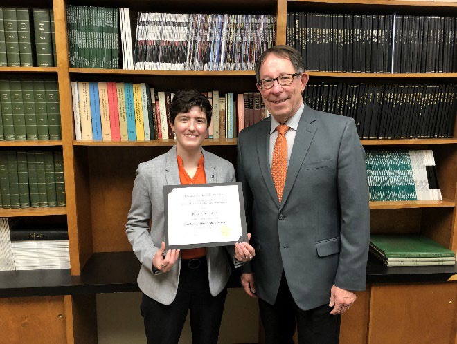 Renee Schuette is accepting her award from Jim Ansley in front of a book shelf.