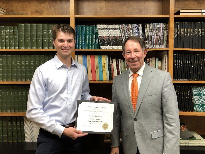 Travis Reddout is accepting his award from Jim Ansley in front of a book shelf